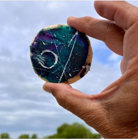 Eclipse-themed iced cookie held against a cloudy sky © Allan Der