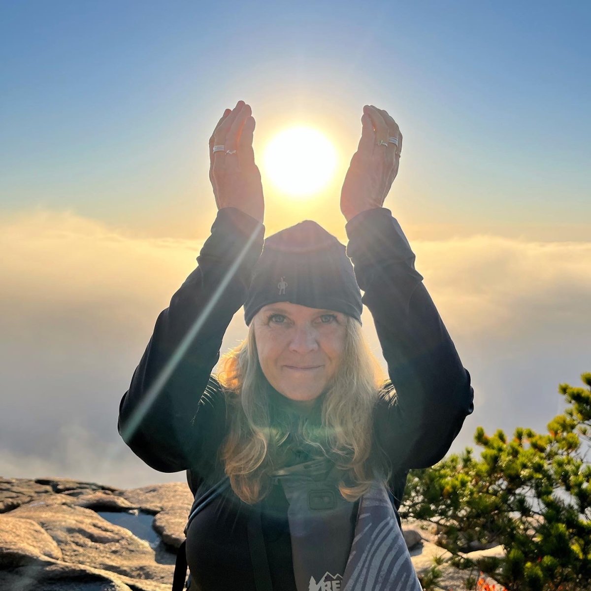 Jennifer poses with hands cupping the morning sun in Acadia National Park