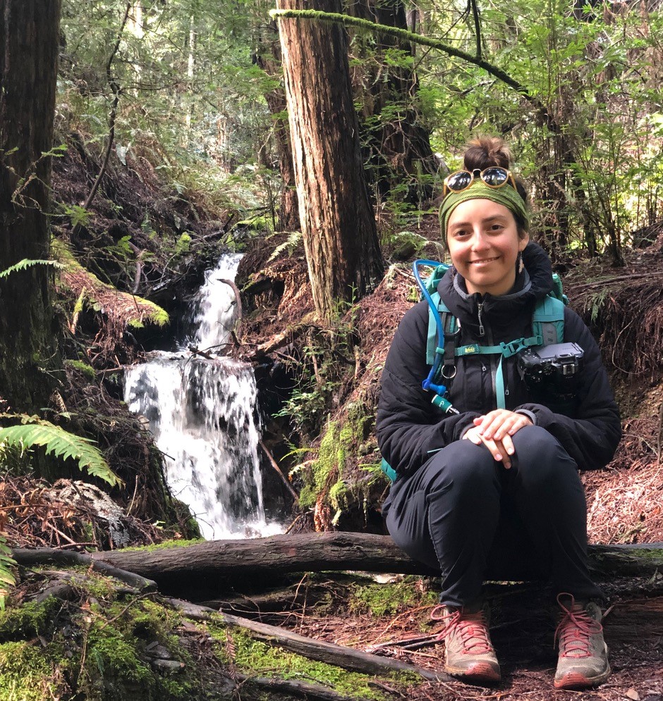Liliana Griego sits on a downed branch with waterfall in the background